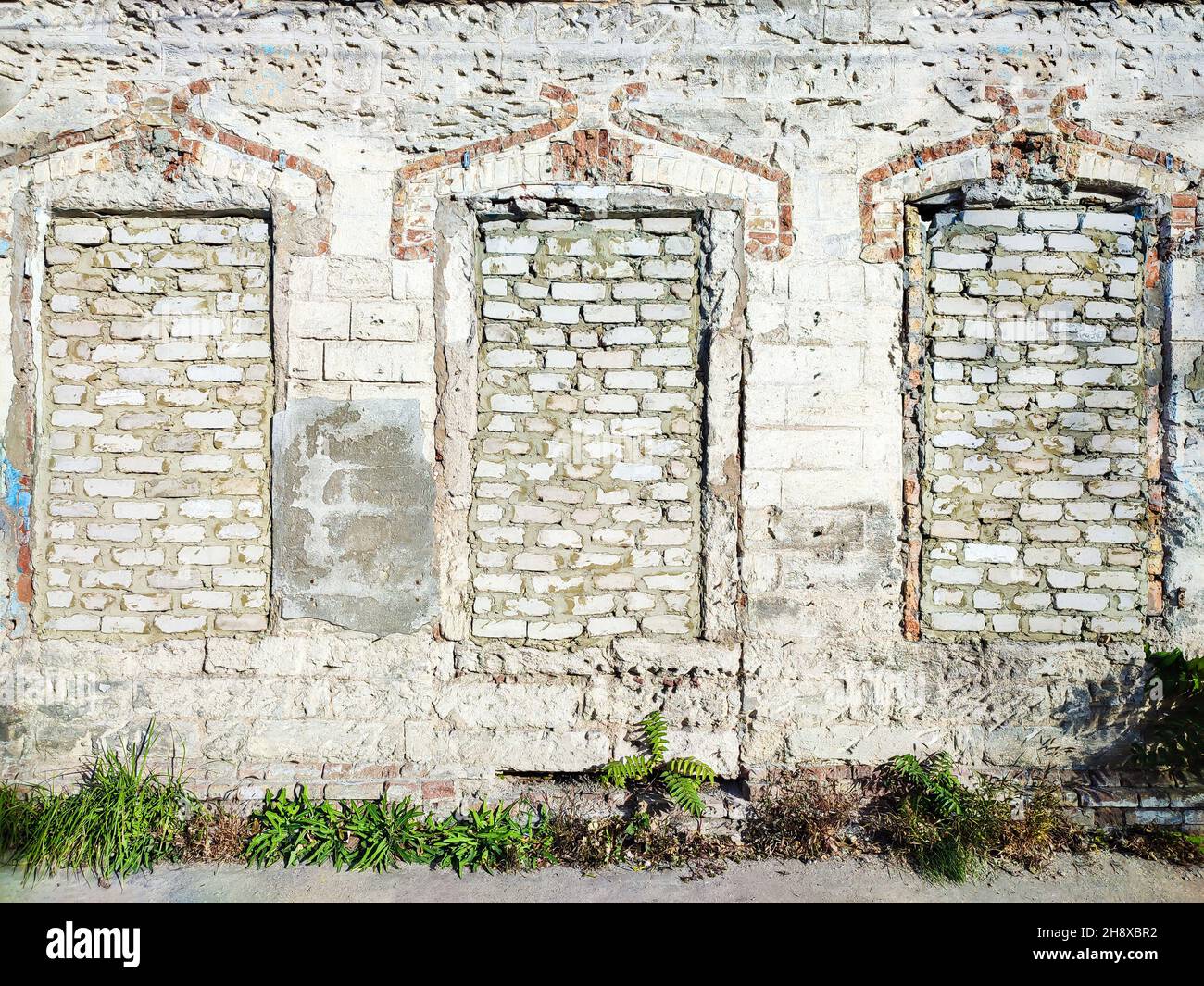 Old white brick wall with three bricked up windows Stock Photo