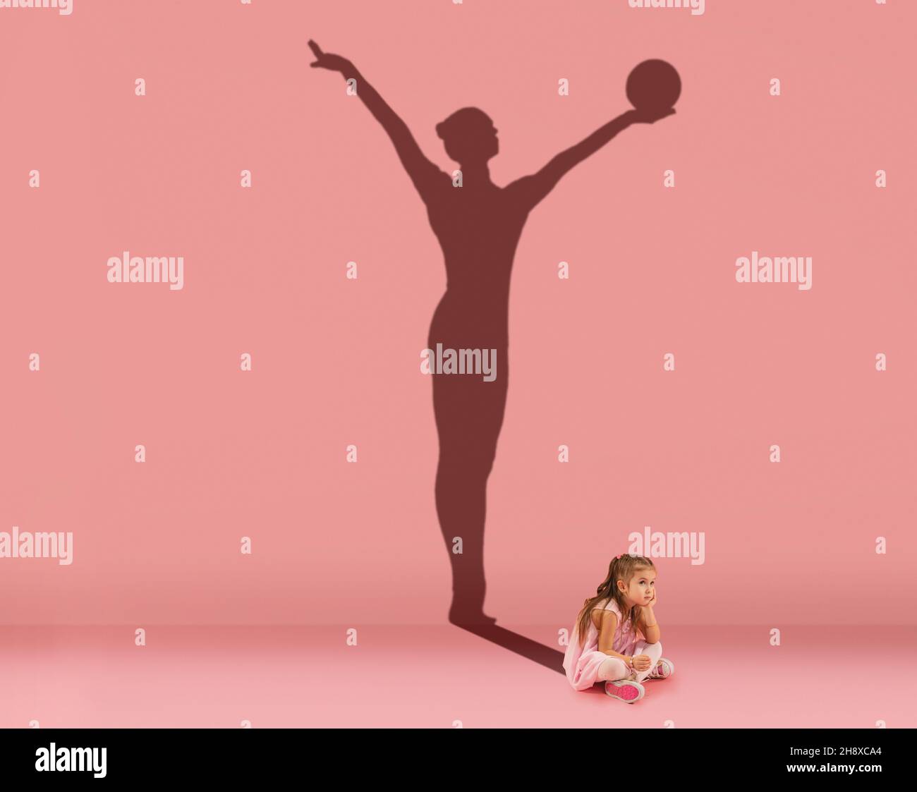 Conceptual image with kid, little girl and shadow of female gymnast on studio pink wall. Dreams about sport career Stock Photo