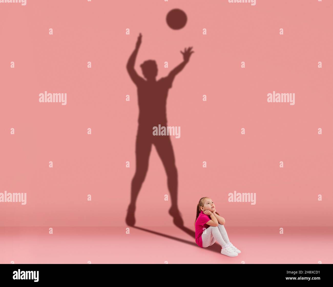 Conceptual image with kid and shadow of female volleyball player on studio wall. Dreams about sport career Stock Photo