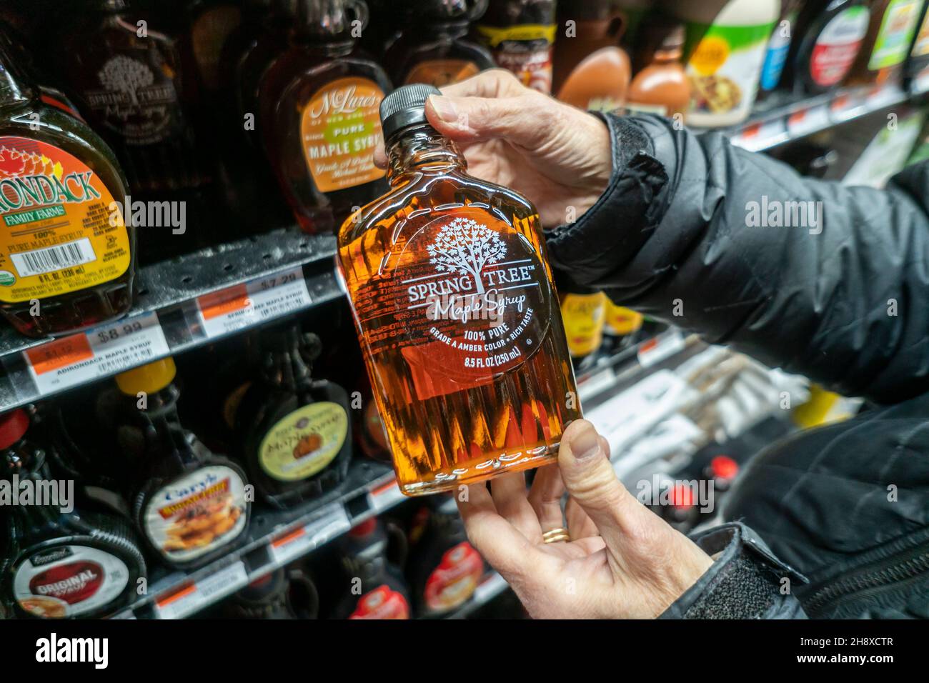 A shopper selects a bottle of maple syrup, a blend of USA and Canadian syrups, in a supermarket in New York on Tuesday, November 30, 2021. Canada has released its strategic maple syrup reserves to prevent a shortfall due to a lower yield this year. Quebec maple syrup producers supply almost 70% of all maple syrup production in the world. (© Richard B. Levine) Stock Photo