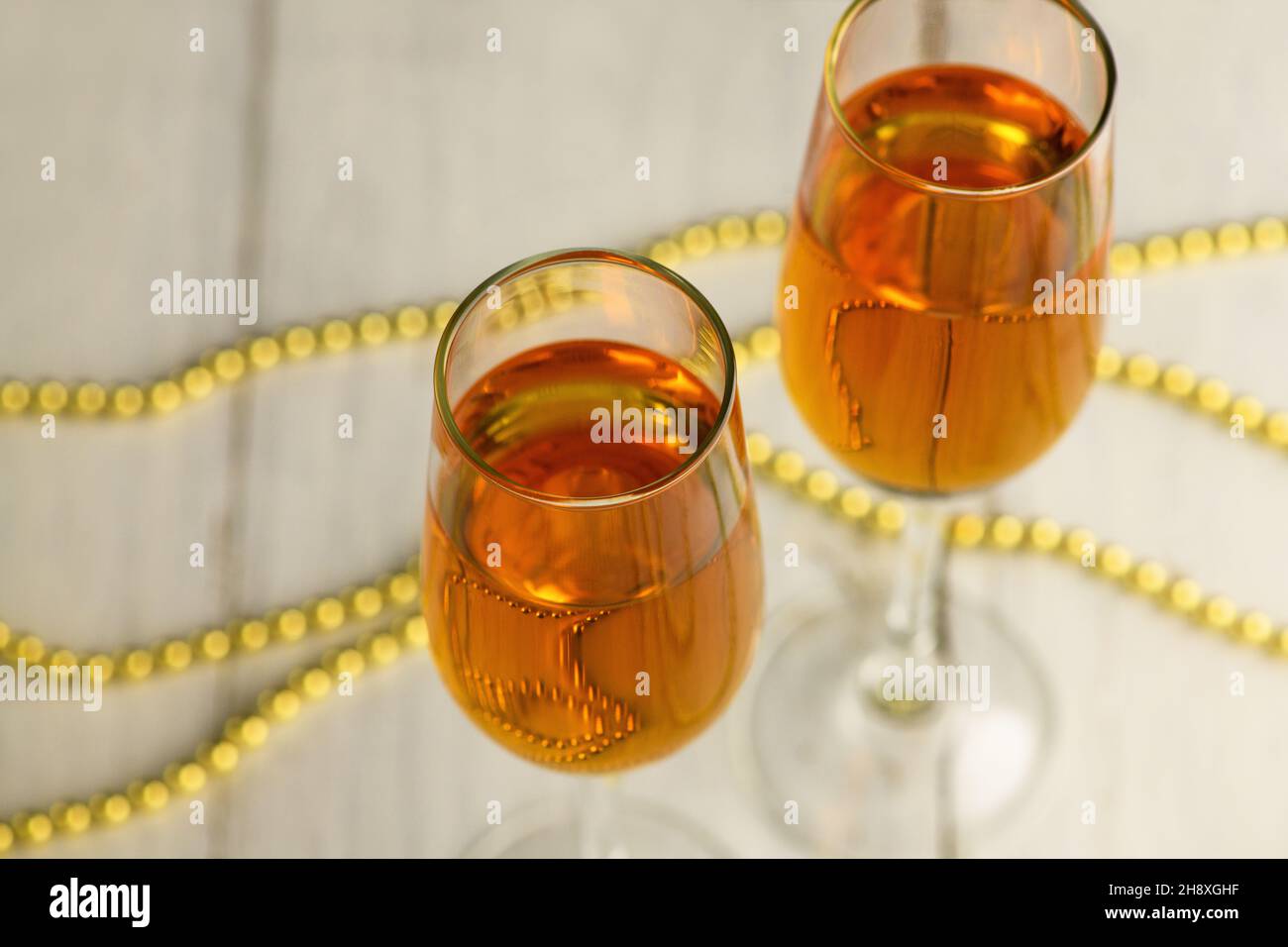 Two glasses of champagne, wine on a light background with gold beads. Alcoholic drink: champagne, beer, white wine. New year and Christmas background. Stock Photo