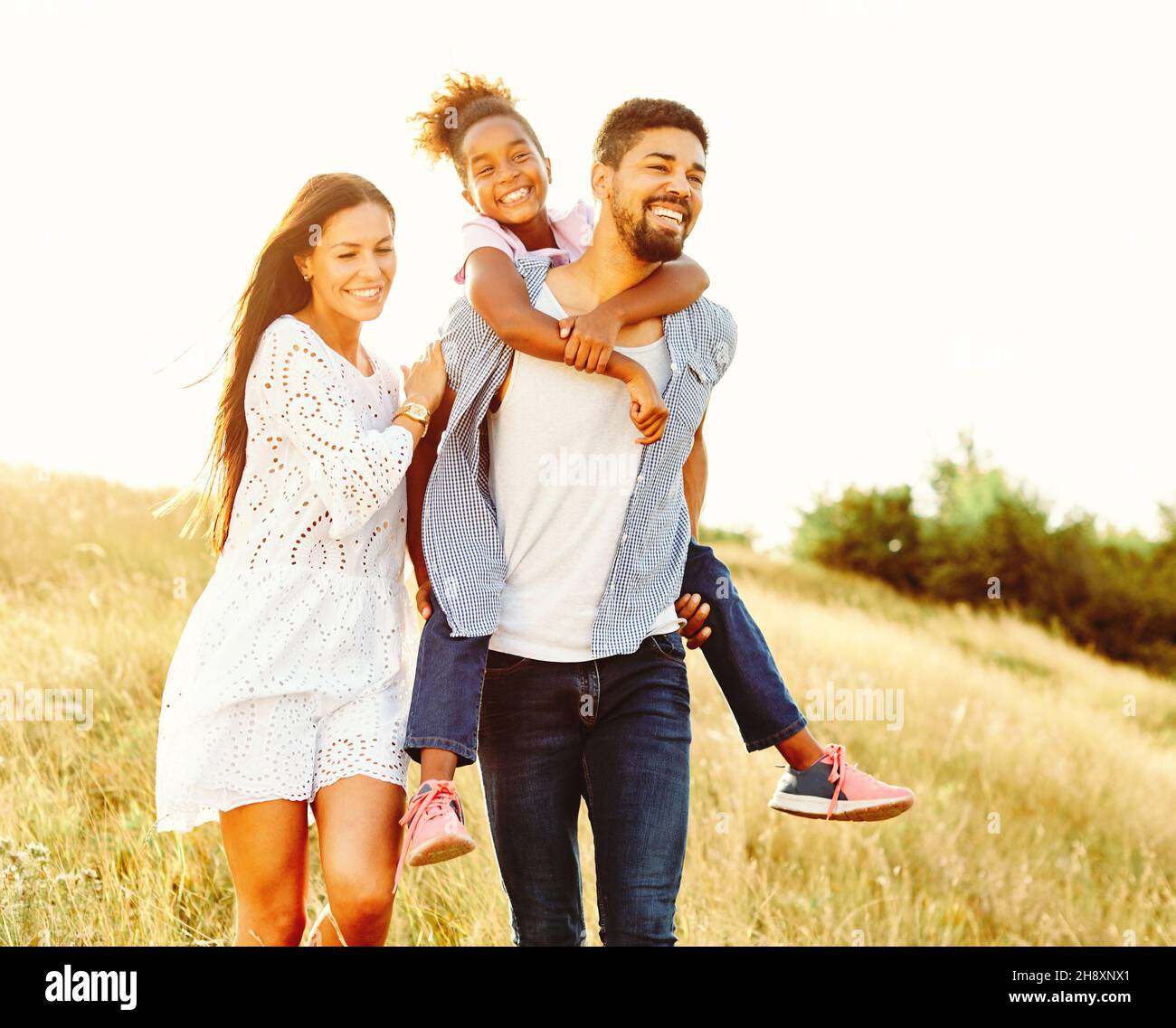 child daughter family happy mother father piggyback fun together girl cheerful field outdoor natur summer Stock Photo