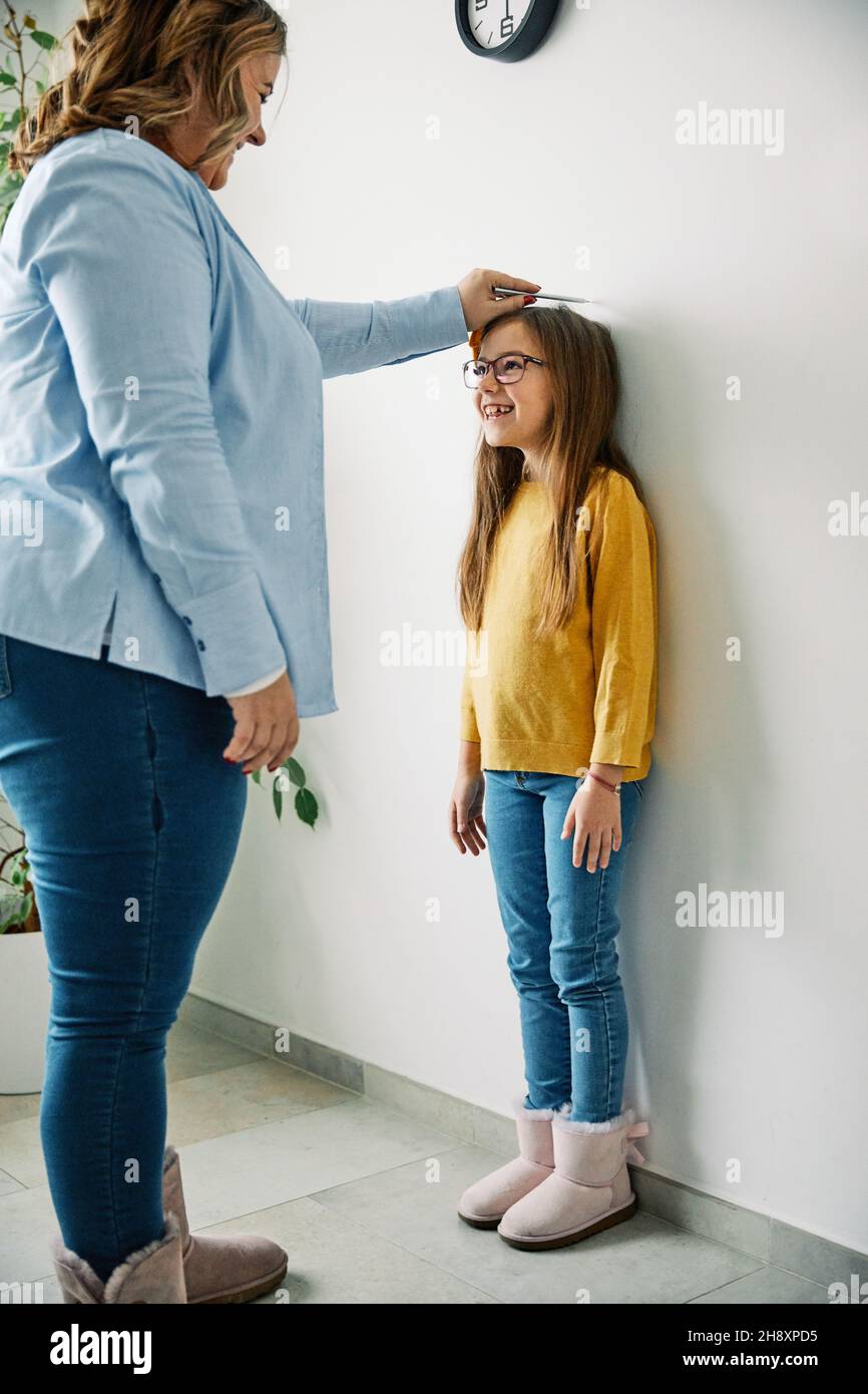 daughter mother measuring height growth childhood tall child heigth kid wall cute Stock Photo