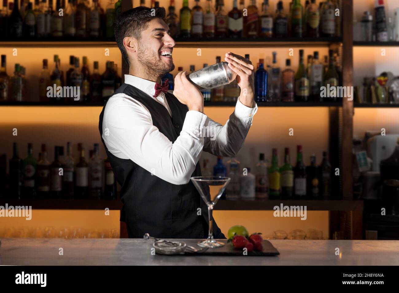 Cool professional bartender making a cocktail, shaking a cocktail shaker. Authentic barman making alcohol beverages in modern bar. High quality photo. Stock Photo