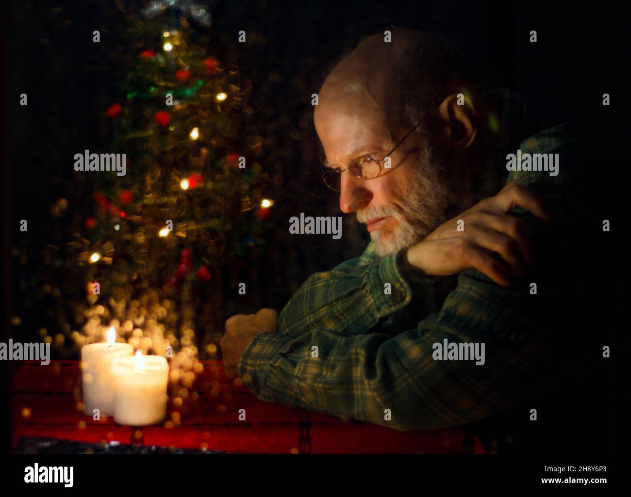 Close-Up Of Thoughtful Senior Man Sitting By Illuminated Christmas Tree At Home Stock Photo