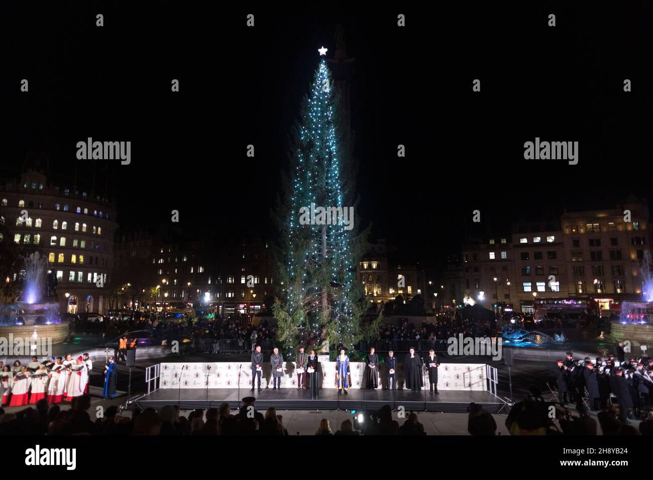 Guests and dignitaries seen singing a hymn on stage, including Mayor of London Sadiq Khan (R4), Lord Mayor of Westminster Councillor Andrew Smith (L3), and Mayor of Oslo Marianne Borgen (R3), during the ceremony.The annual Trafalgar Christmas Tree Ceremony has taken place since the 1947s. A giant Norwegian spruce, standing at 25 meters tall, is gifted by the people of Norway to London in recognition of Britain's support during the Second World War. The Christmas tree is lit up during the ceremony, with choirs and bands performing Christmas Carols. Stock Photo