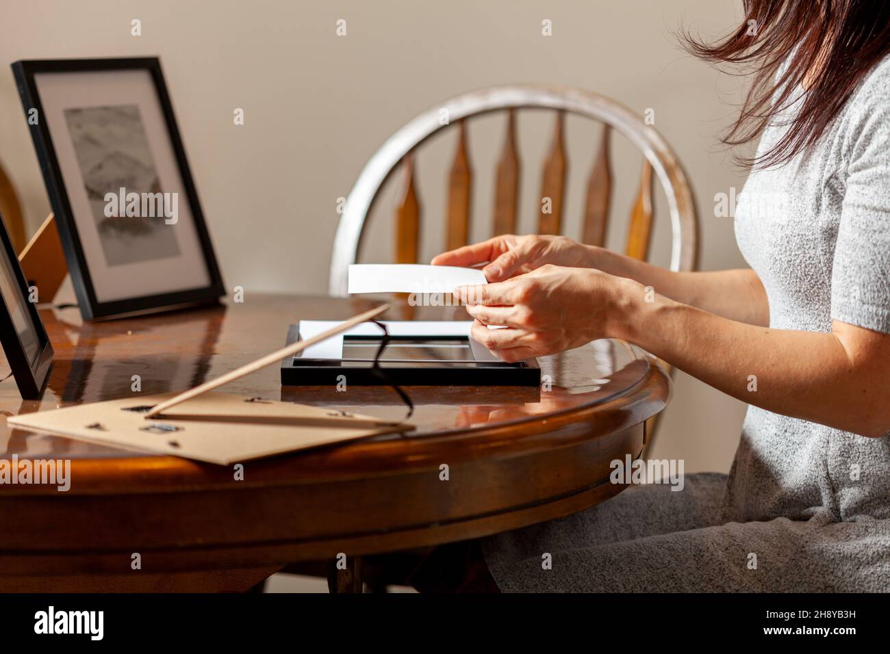 A young caucasian woman is placing a printed photograph into a picture frame with kickstand. There are other frames on the table. Tabletop picture fra Stock Photo
