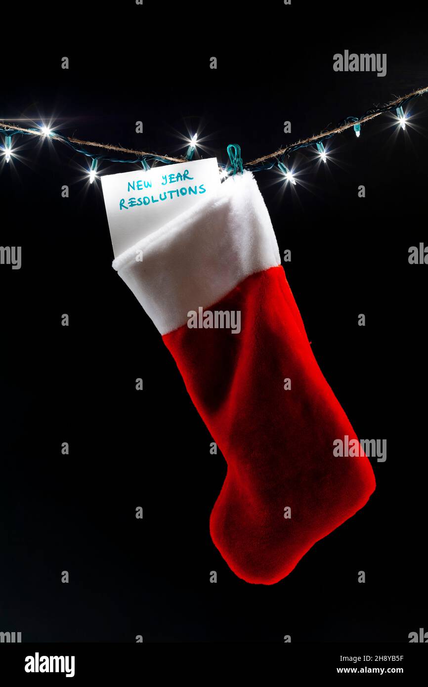 A new year's resolutions list is attached to a christmas stocking hanging on a string of decorative lights. A dark humor concept image for responsibil Stock Photo