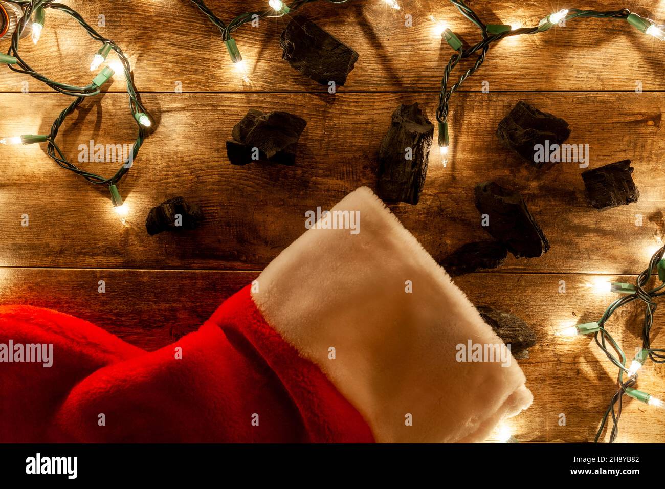 naughty kid who do not behave get coal for christmas concept. Coal pieces go out of christmas stocking o wooden background with string lights around i Stock Photo