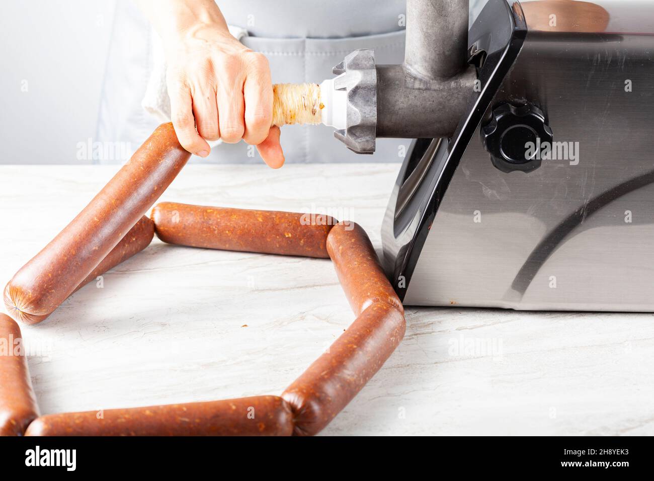 a woman cook wearing apron is stuffing homemade sucuk or sausage into casing using an electrical meat grinder and stuffer. This is an healthier preser Stock Photo