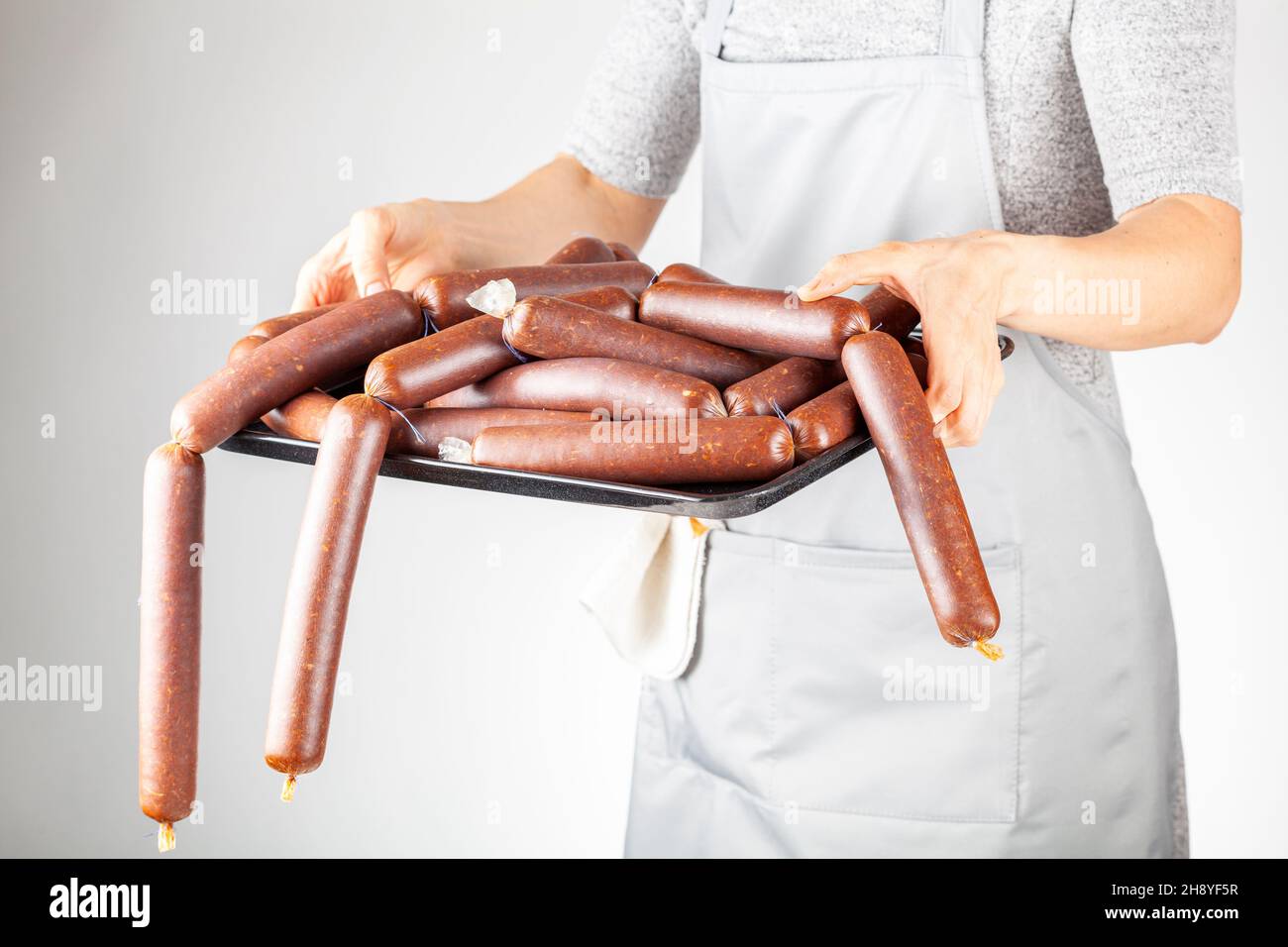 A woman chef is showing a heap of homemade Turkish sucuk or sausage on a tray. Processed fermented spicy red meat consumption concept. Stock Photo