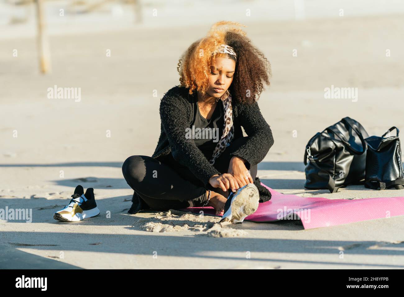 Pregnant woman taking off the shoes sitting on a yoga mat on a beach