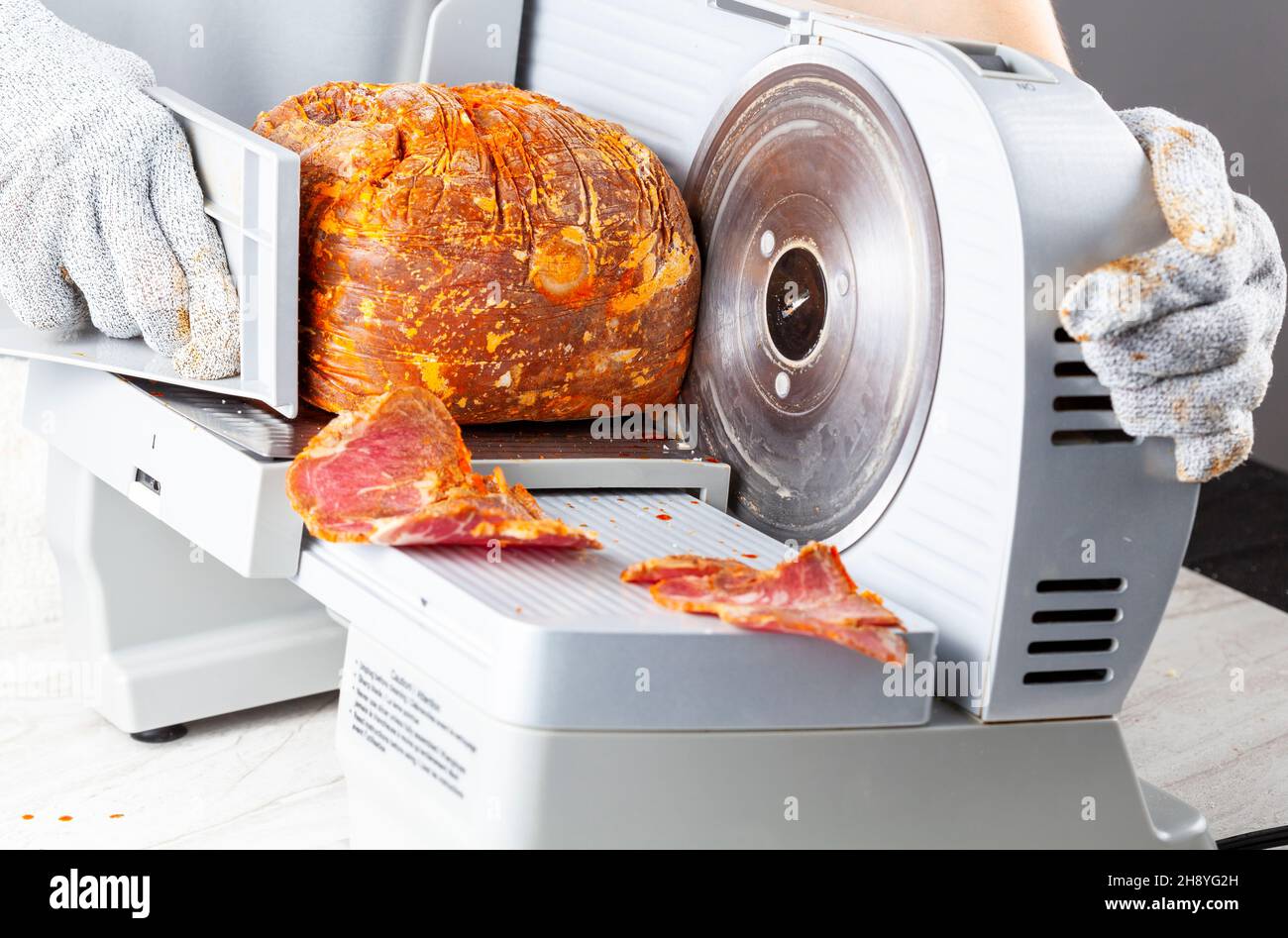 Close up isolated image showing a butcher or chef slicing a large frozen cured meat block. Turkish pastirma, pastrami, ham, beef concept. The person w Stock Photo