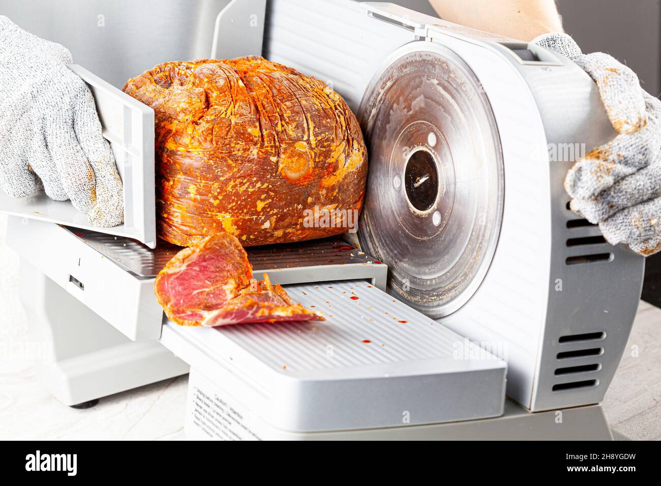 Close up isolated image showing a butcher or chef slicing a large frozen cured meat block. Turkish pastirma, pastrami, ham, beef concept. The person w Stock Photo
