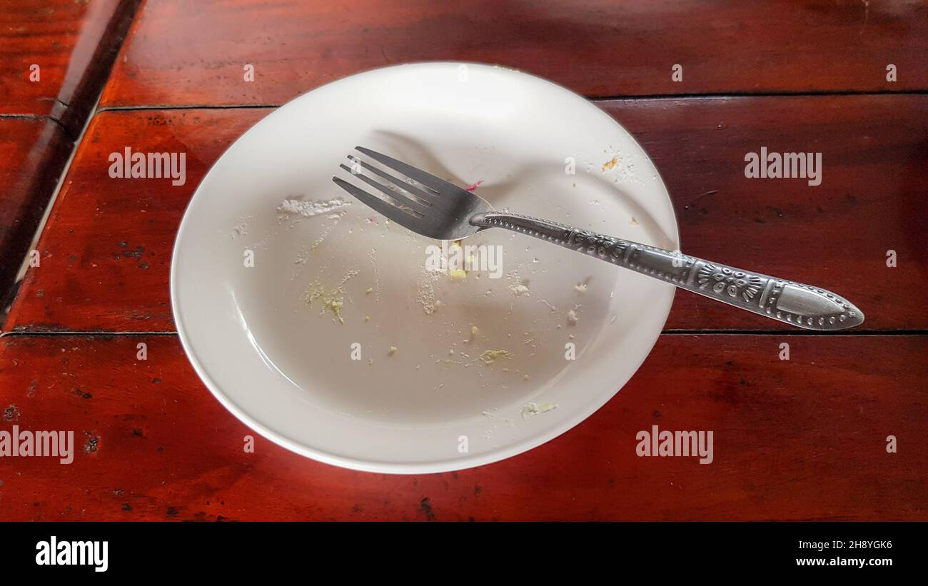 The plate left over from eating the cake had a piece of cake stuck to the plate and a fork was placed on the plate before being washed. Stock Photo