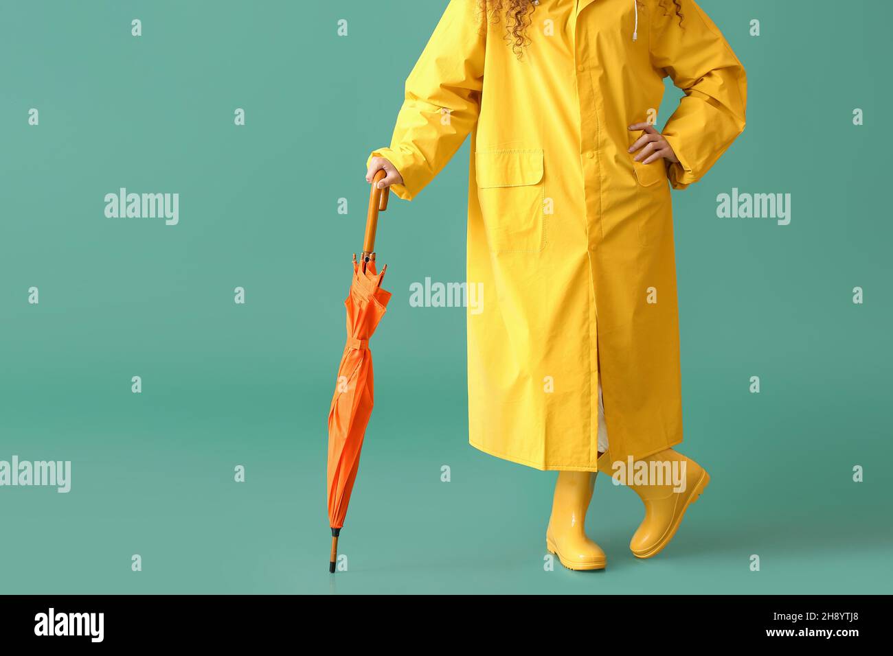 Young woman wearing yellow raincoat and gumboots with umbrella on green