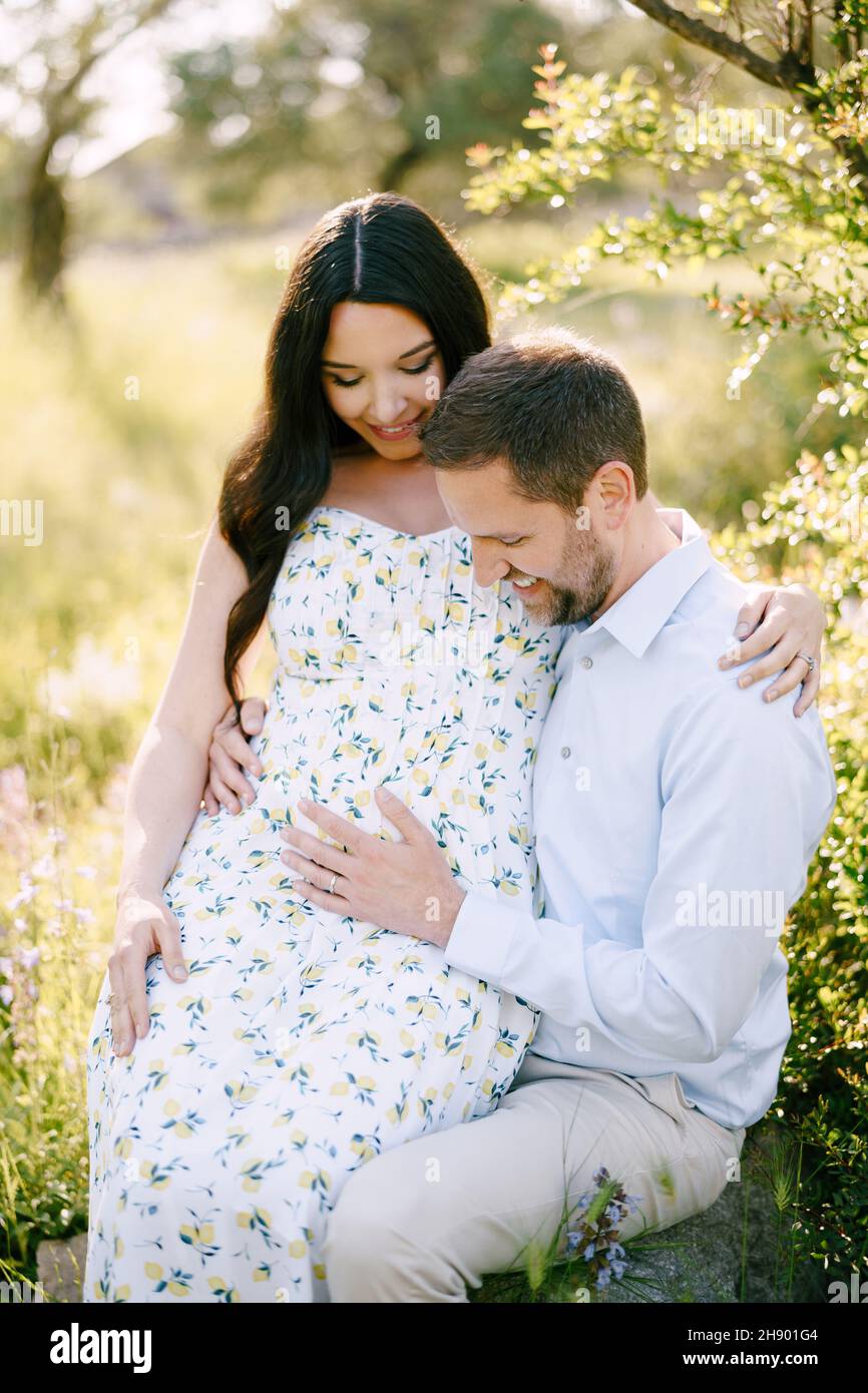 Man holds his hands on the belly of a pregnant woman sitting on his lap