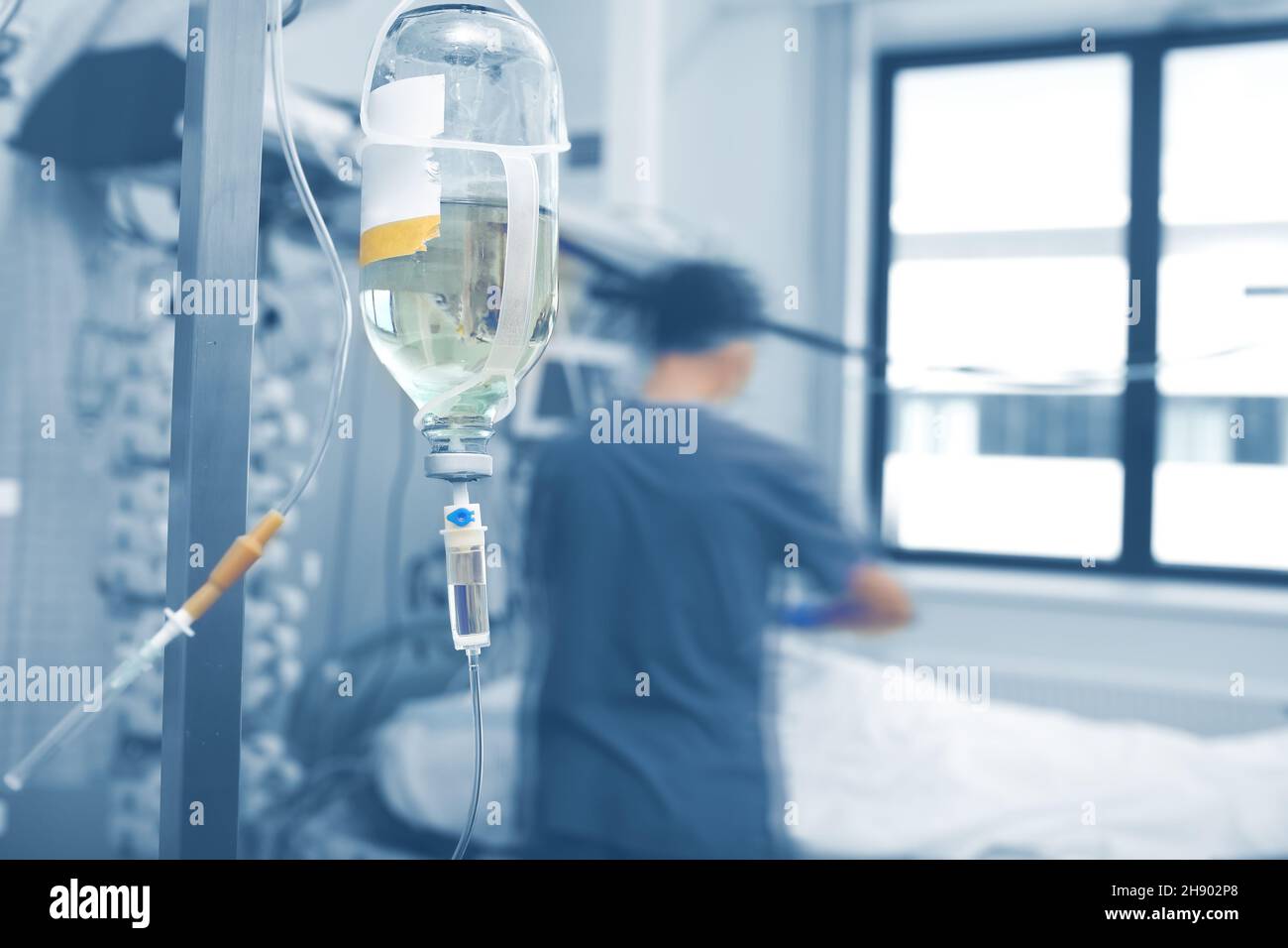 Intravenous infusion bottle hanging on the pole agienst the blurred silhouette of male medical worker. Stock Photo