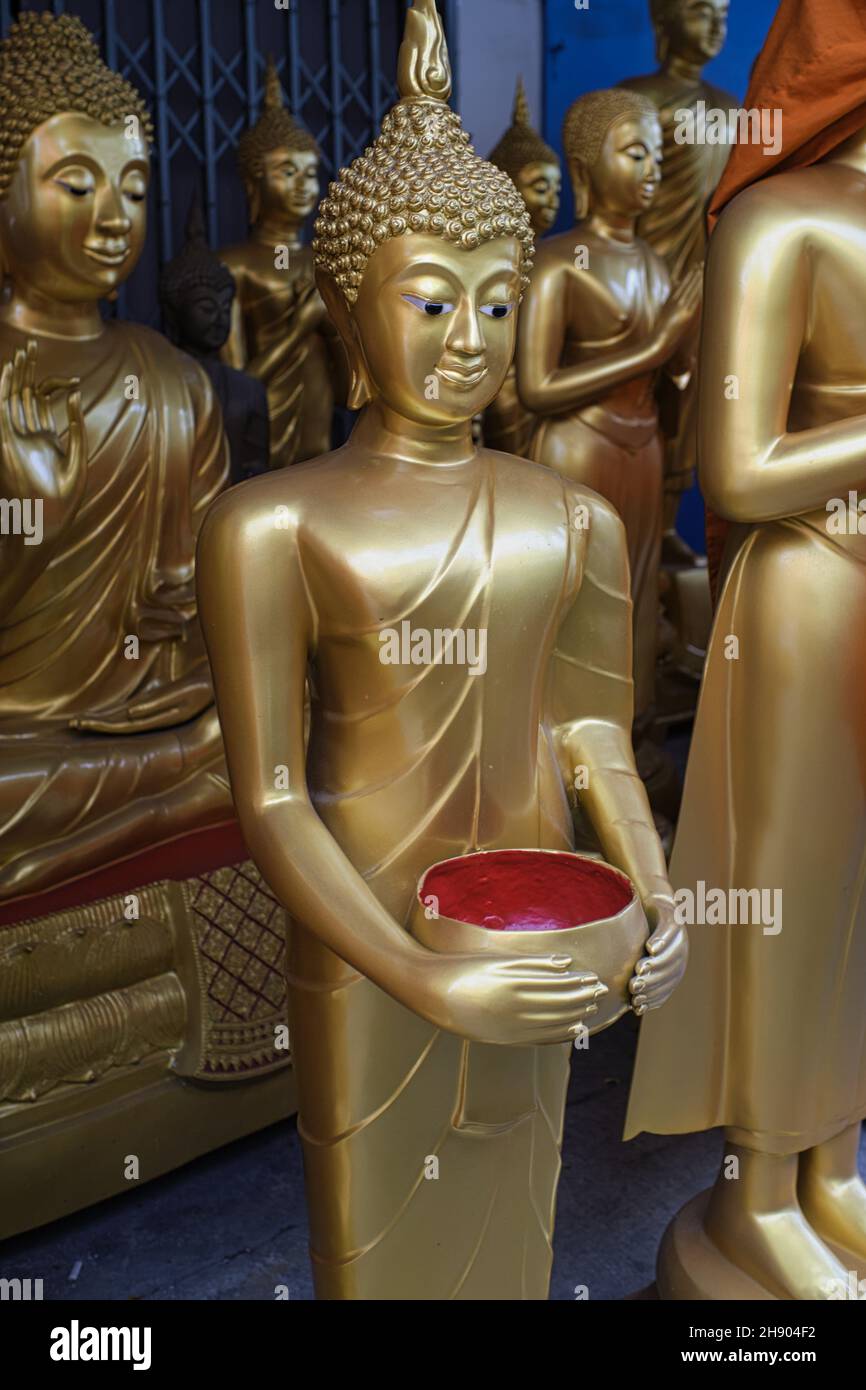 Buddha statues at a factory for Buddhist objects in Bamrung Muang Rd., Bangkok, Thailand, one statue holding an alms' bowl as used by Buddhist monks Stock Photo