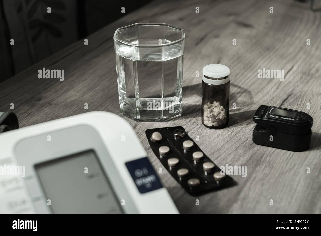 Close-up of a glass of water, pills, a device for measuring blood pressure and oxyometer. Black and white photo. The concept of health Stock Photo