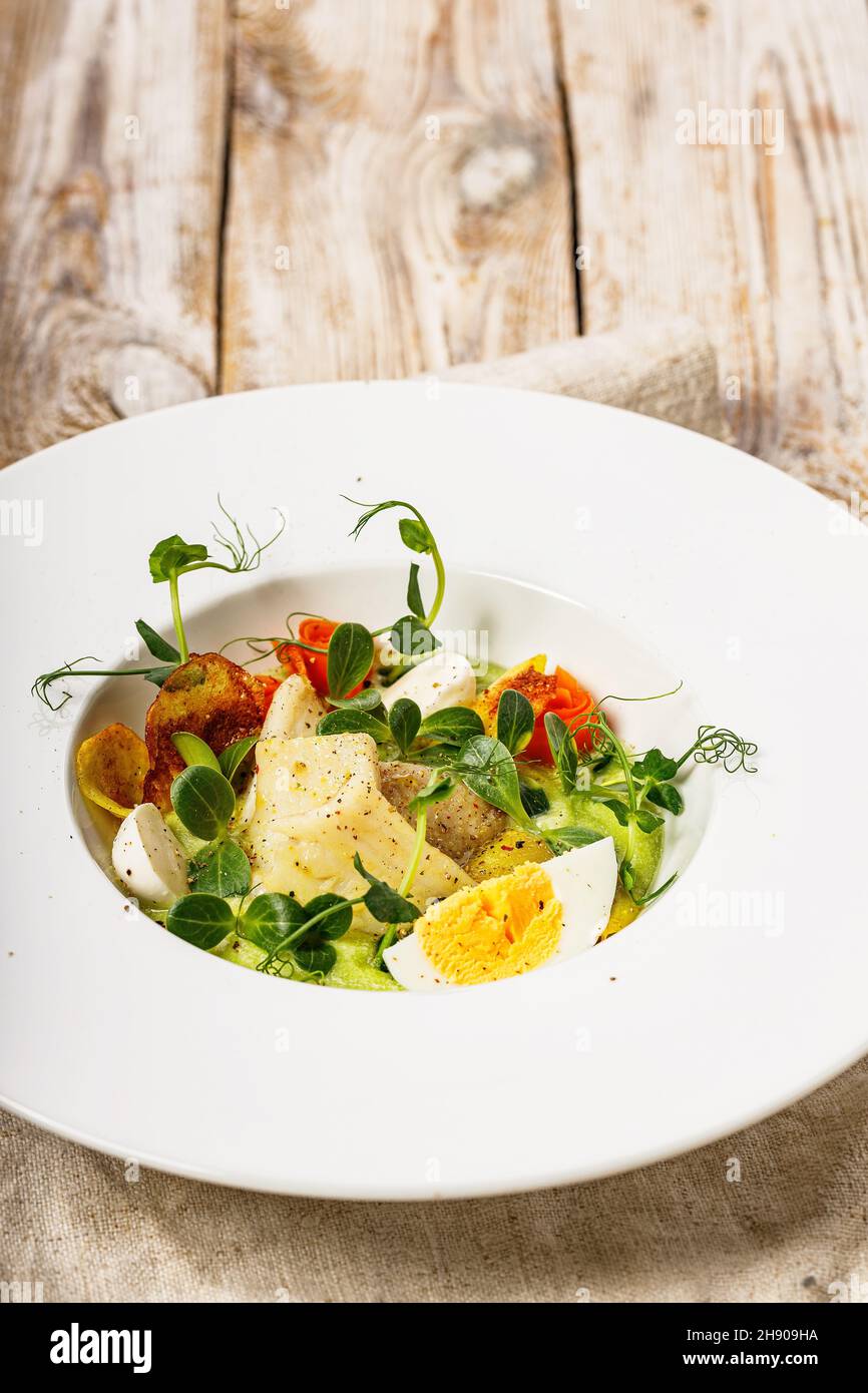Close-up gourmet fish salad. Cod fillet, vegetables, avocado pate and fresh herbs. Restaurant serving. Chef's dish. Healthy and tasty food on a light Stock Photo