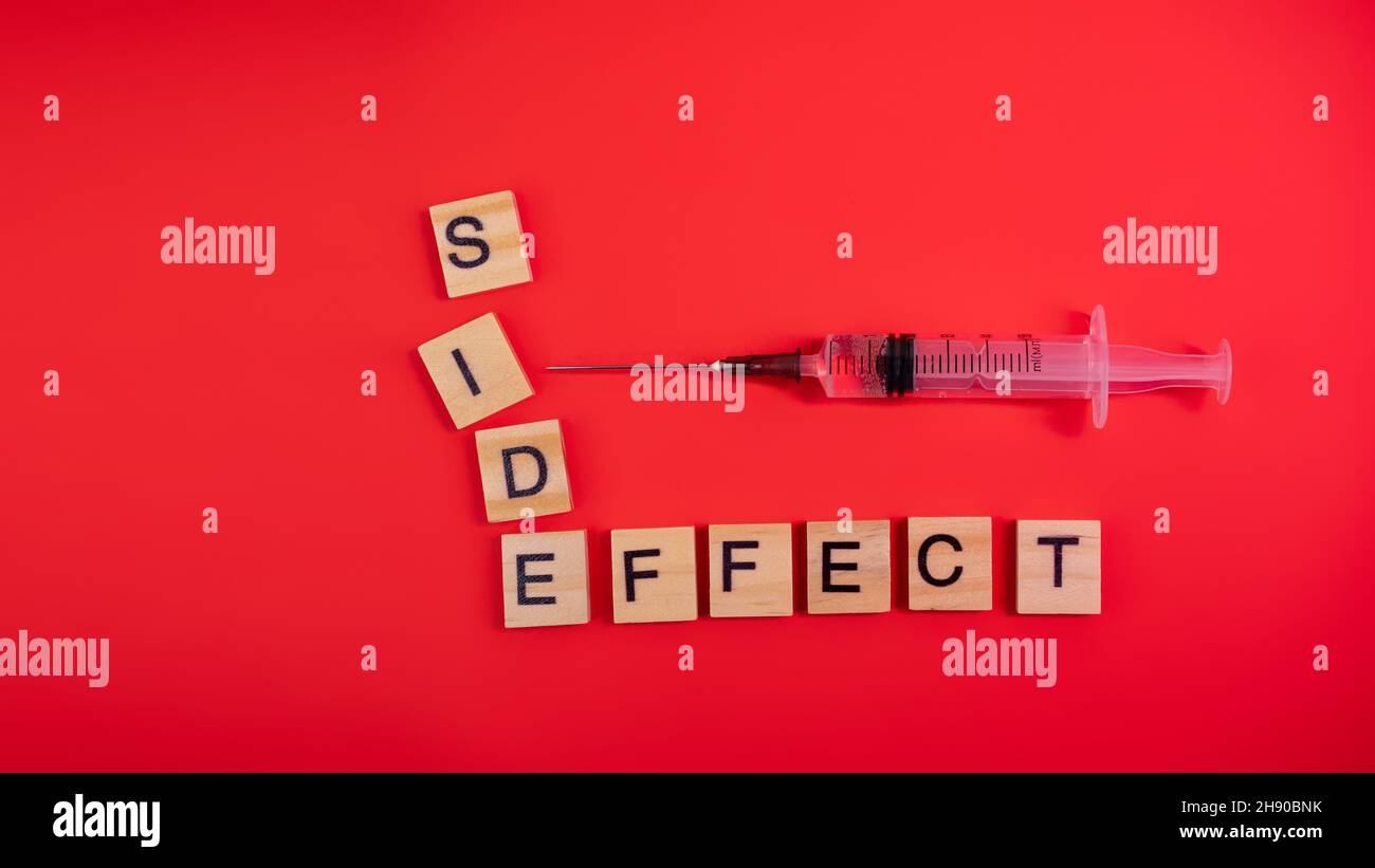 Syringe filled with solution. Words side effect on colored red paper ...