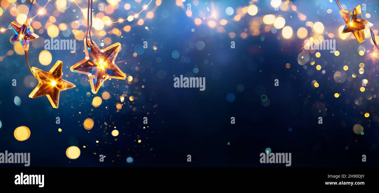 Christmas Stars Lights - Golden String Hanging In Blue Background With Abstract Defocused Bokeh Stock Photo