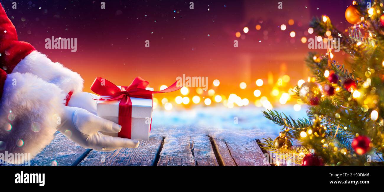 Santa Claus Putting Gift Present Below Christmas Tree With Abstract Lights At Night Stock Photo
