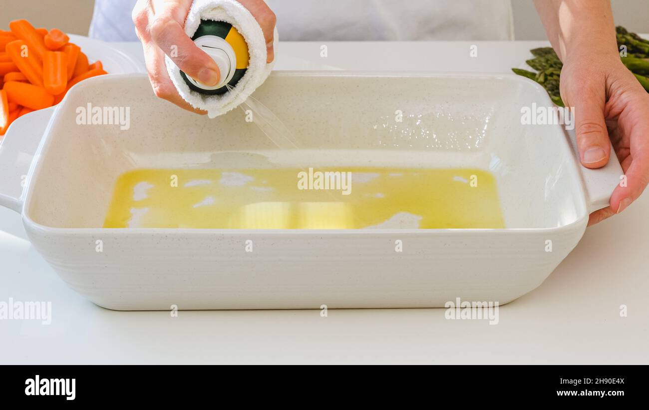 Woman using olive oil spray on a white ceramic baking dish. Cooking