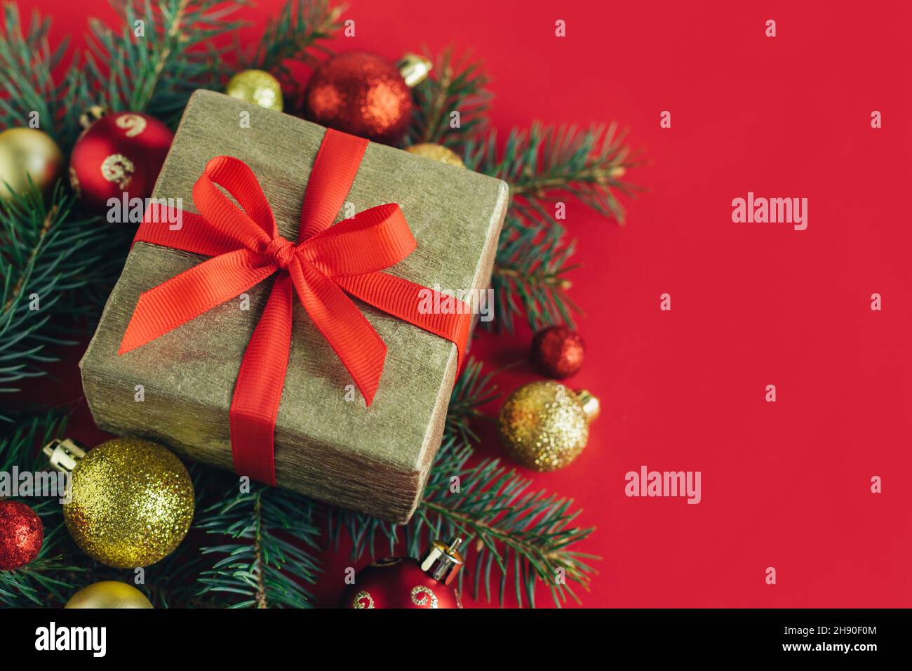 Gift box with spruce branches, red and golden balls on a red background ...
