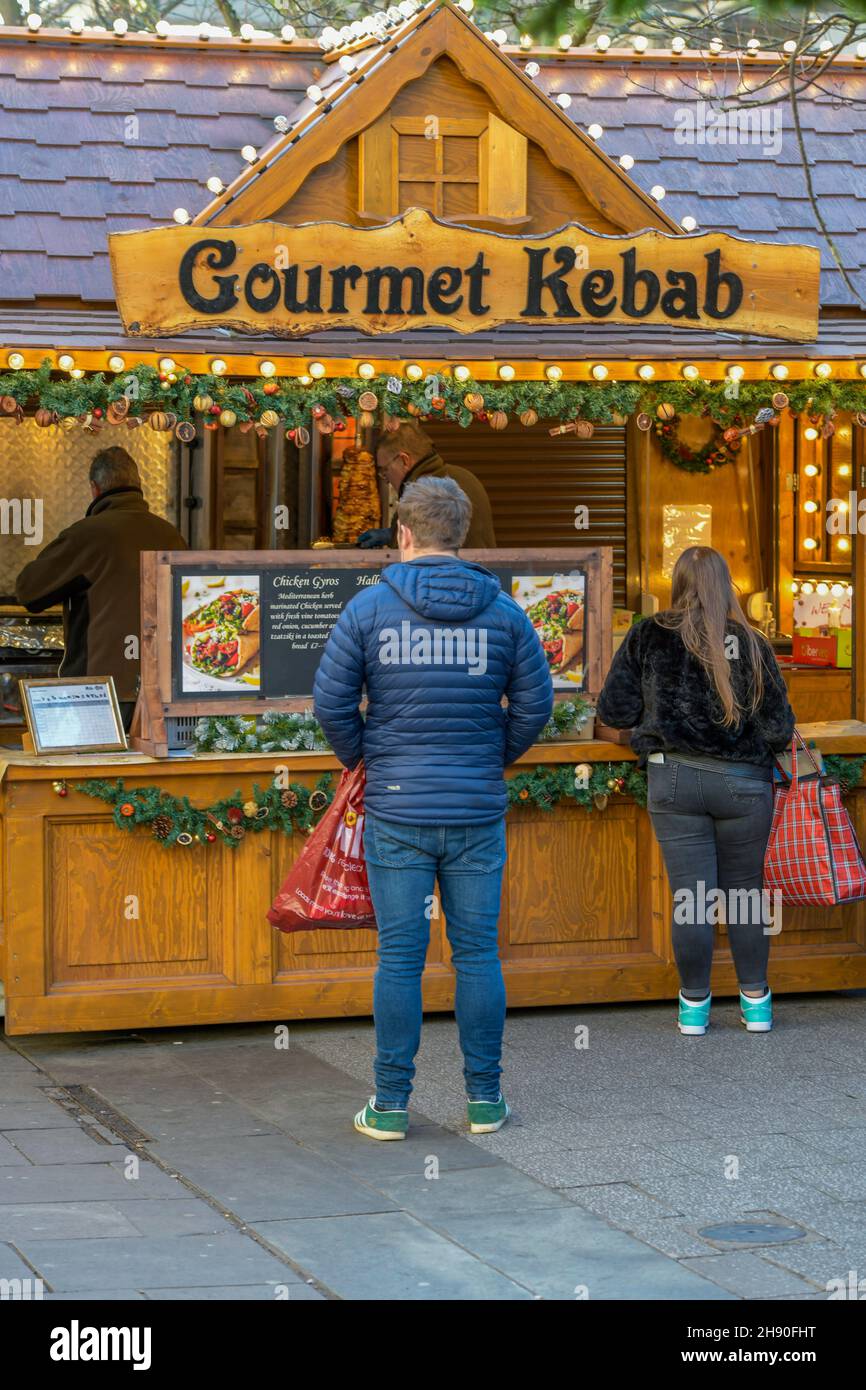 man and woman queueing at a kebab fast food stall at a christmas market, gourmet kebabs takeaway foods market stand, kebabs and hot foods market stall Stock Photo