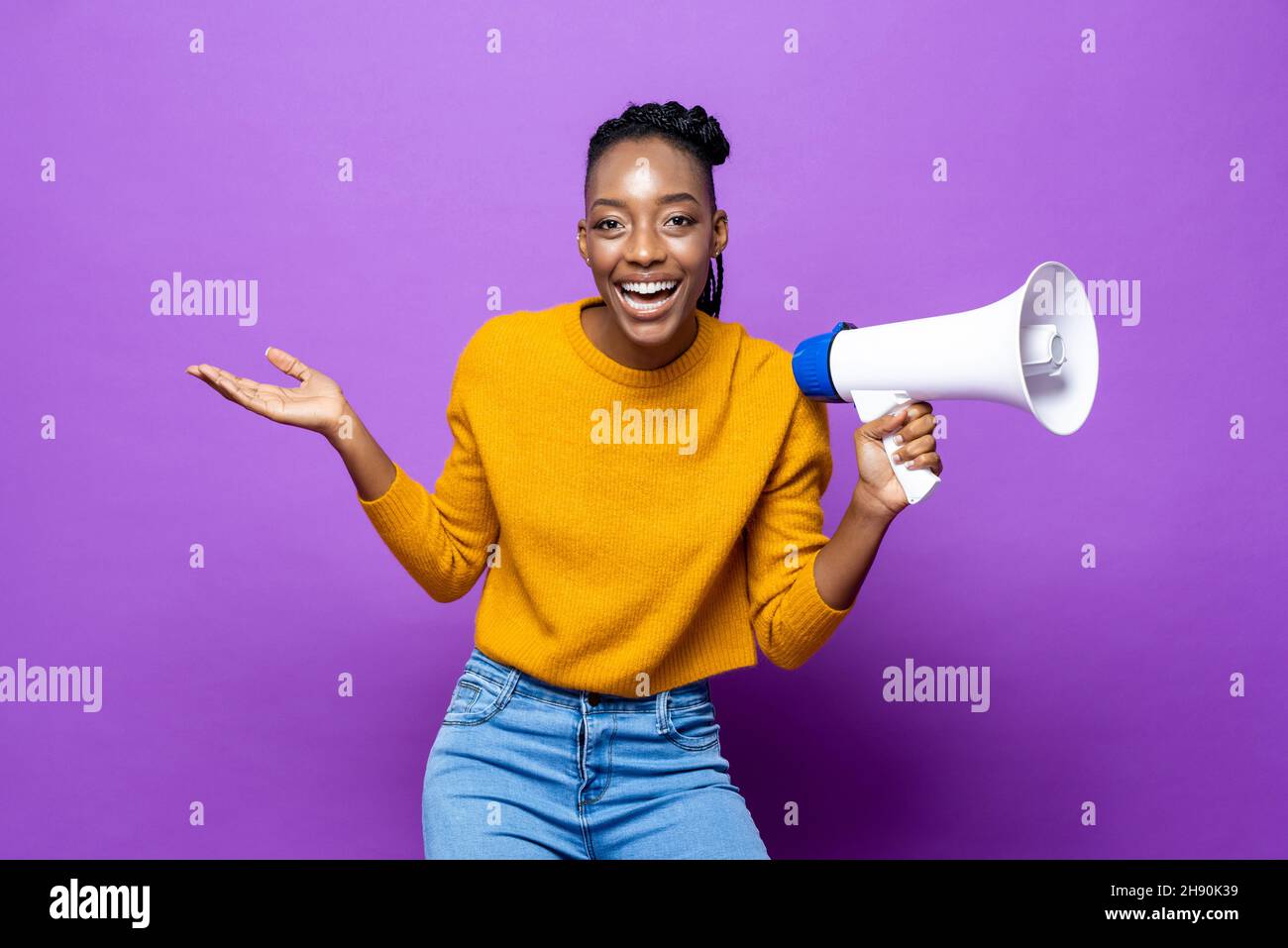 Young smiling African-American woman holding megaphone with another hand open in purple studio isolated background Stock Photo