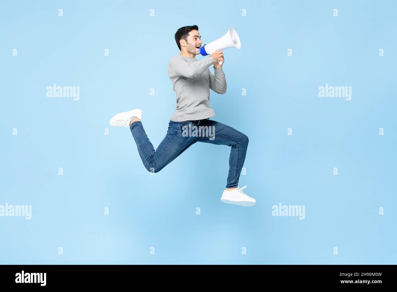 Portrait of energetic young Caucasian man jumping with megaphone isolated on light blue background Stock Photo