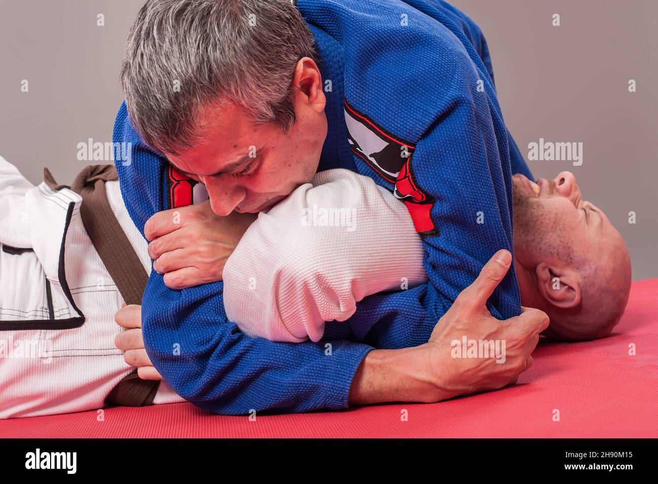 Kapap and brazilian jiu jitsu instructor in traditional kimono demonstrates ground fighting arm lock techniques with his student Stock Photo