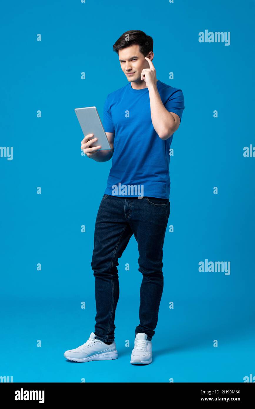 Young handsome Caucasian man holding tablet computer and pointing finger on head in isolated a light blue studio background Stock Photo