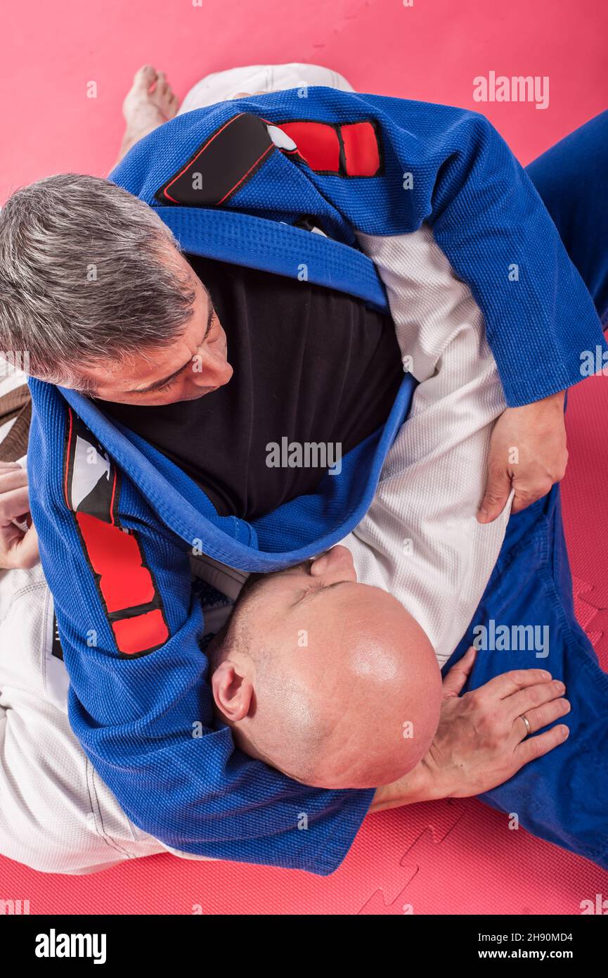 Kapap and brazilian jiu-jitsu instructor in traditional kimono demonstrates ground fighting techniques with his student Stock Photo