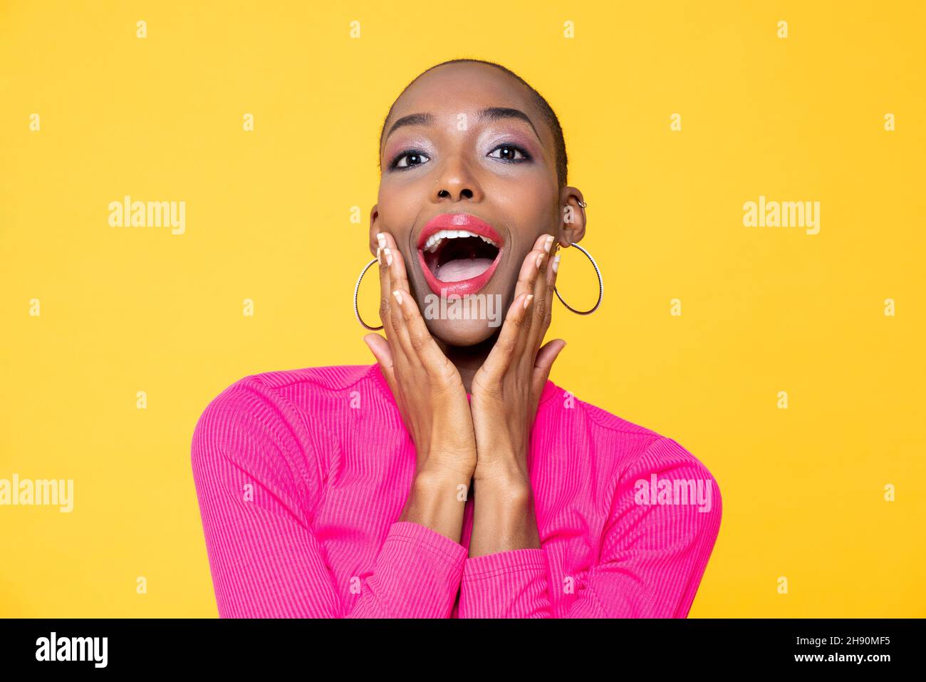 Close up portrait of surprised young African American woman with hands on cheeks isolated on studio yellow background Stock Photo