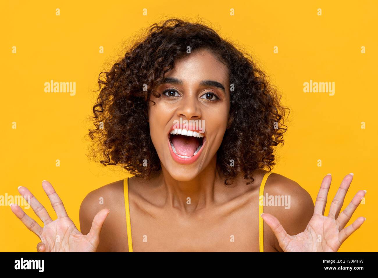 Happy smiling curly hair beautiful woman looking at camera with opsn mouth isolated on yellow background Stock Photo