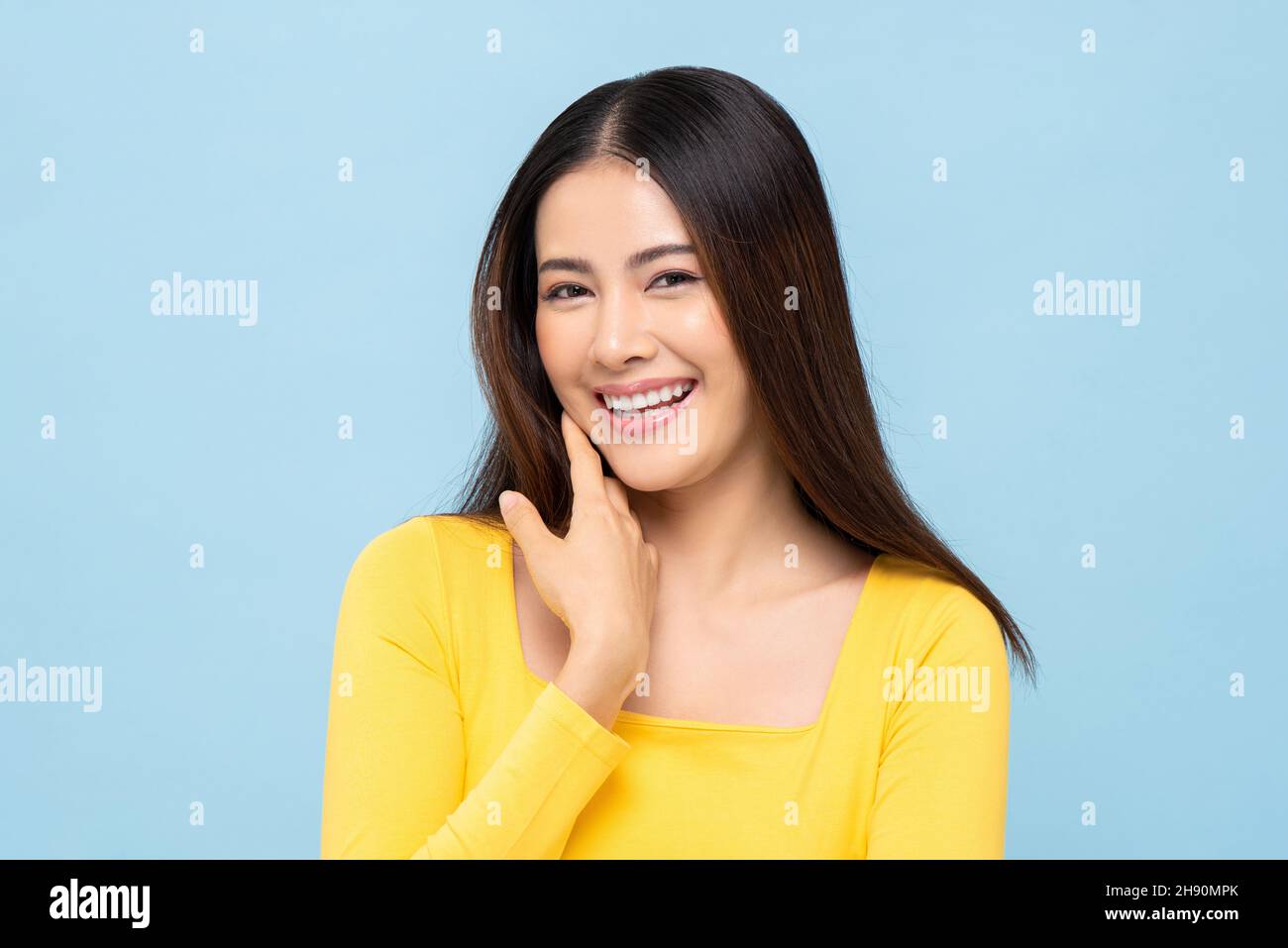 Beautiful smiling young Asian woman face in light blue isolated studio background Stock Photo