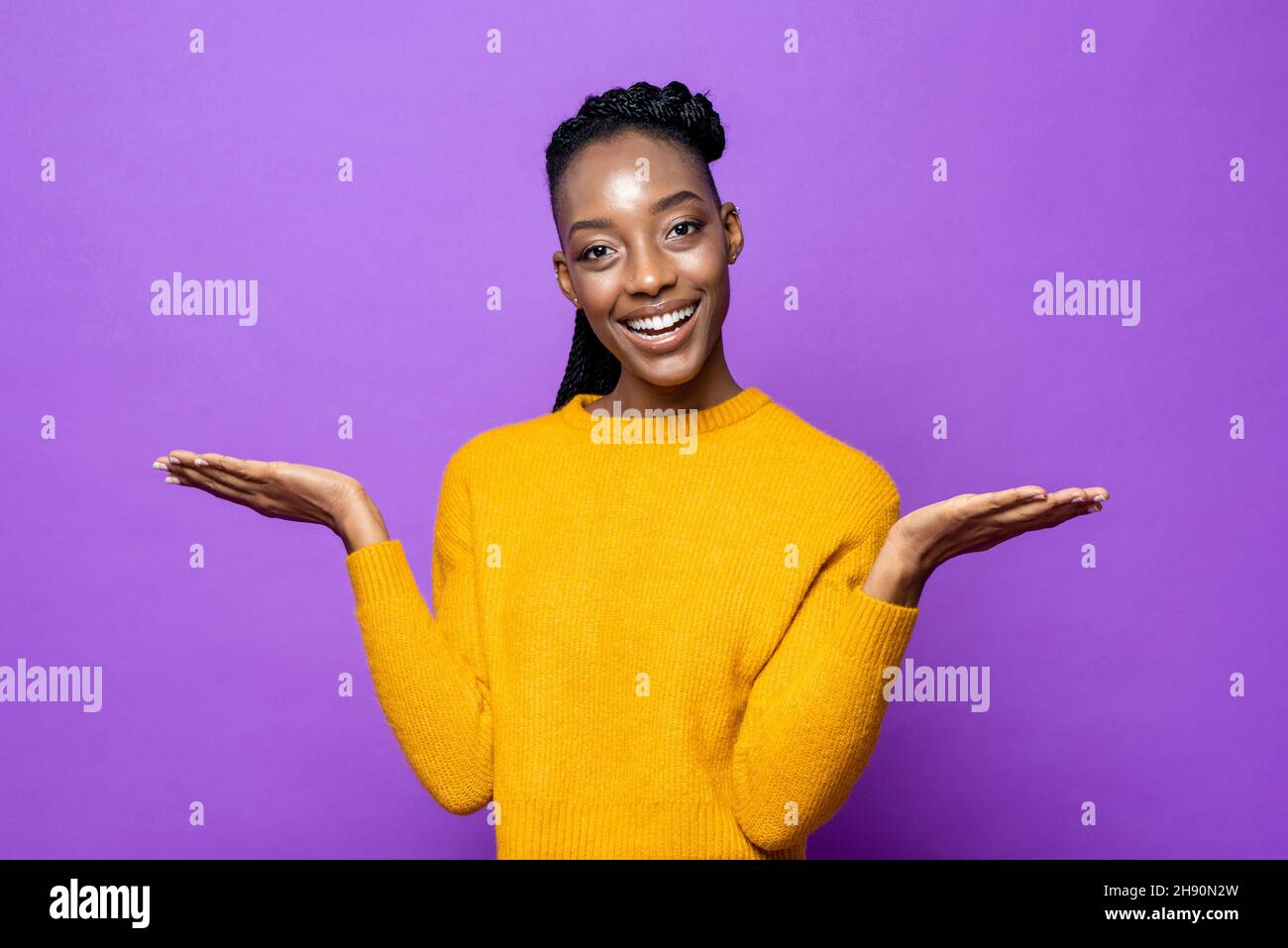 Smiling young African American woman opening hands to empty space in isolated purple studio background Stock Photo