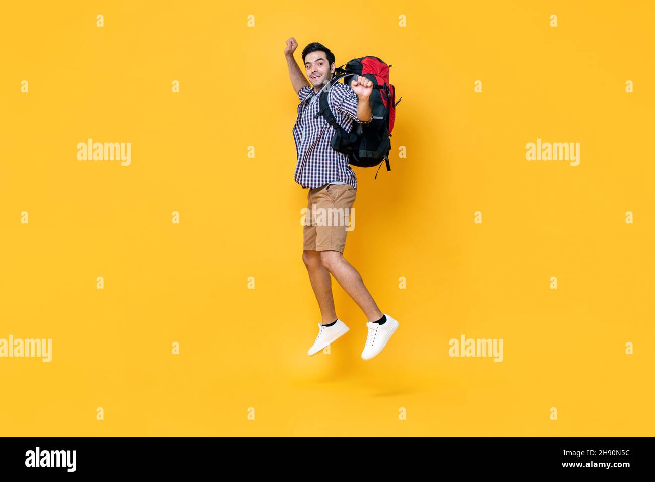 Portrait of excited young Caucasian male tourist backpacker jumping in mid-air isolated on yellow studio background for travel and vacation concept Stock Photo