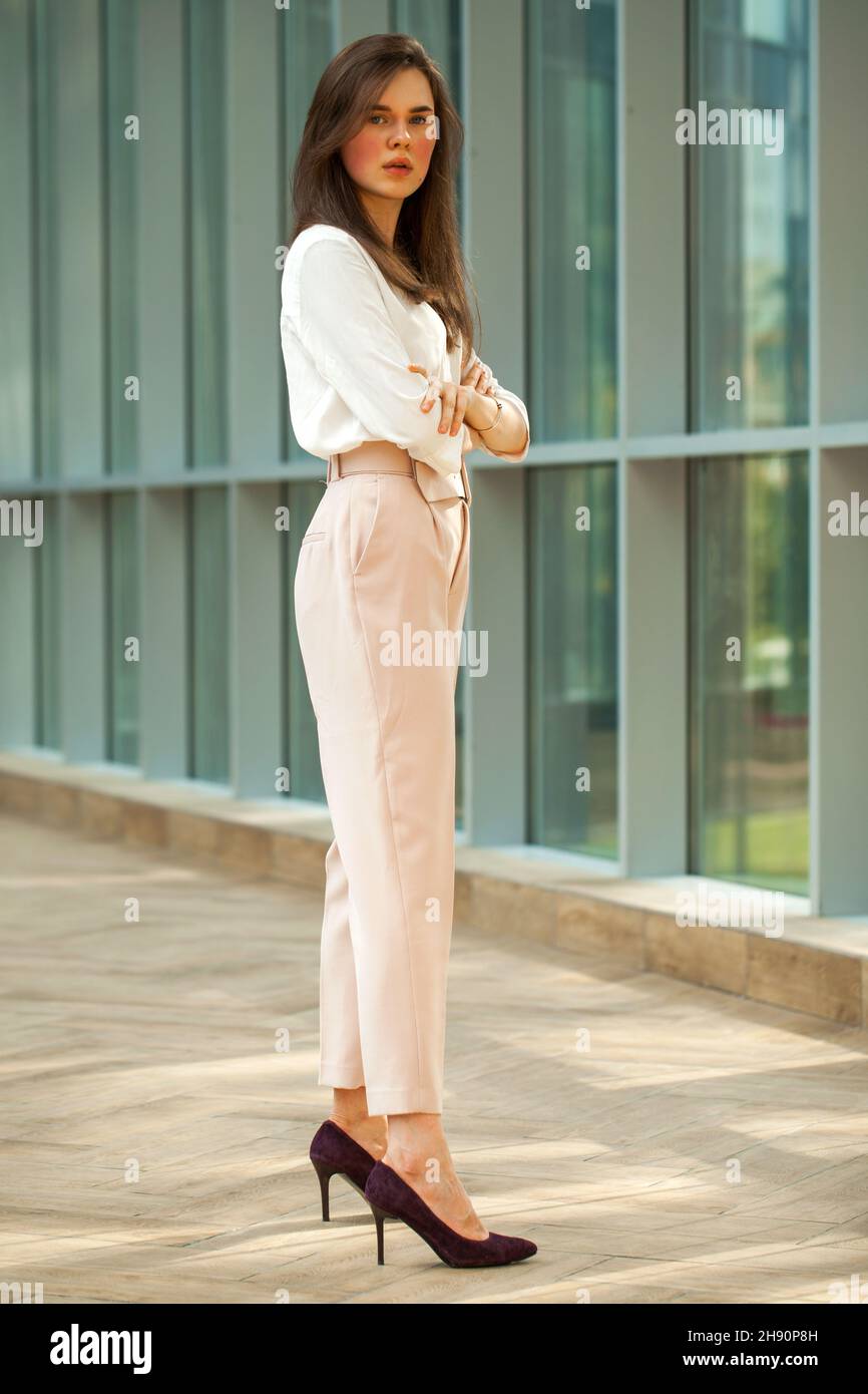 Full-length portrait young beautiful brunette woman in white blouse and pink  pants in office Stock Photo - Alamy