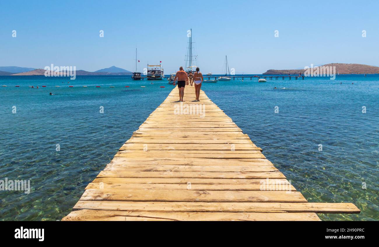 Couple walking down wooden pier at Camel Beach near Bodrum, Turkey Stock Photo