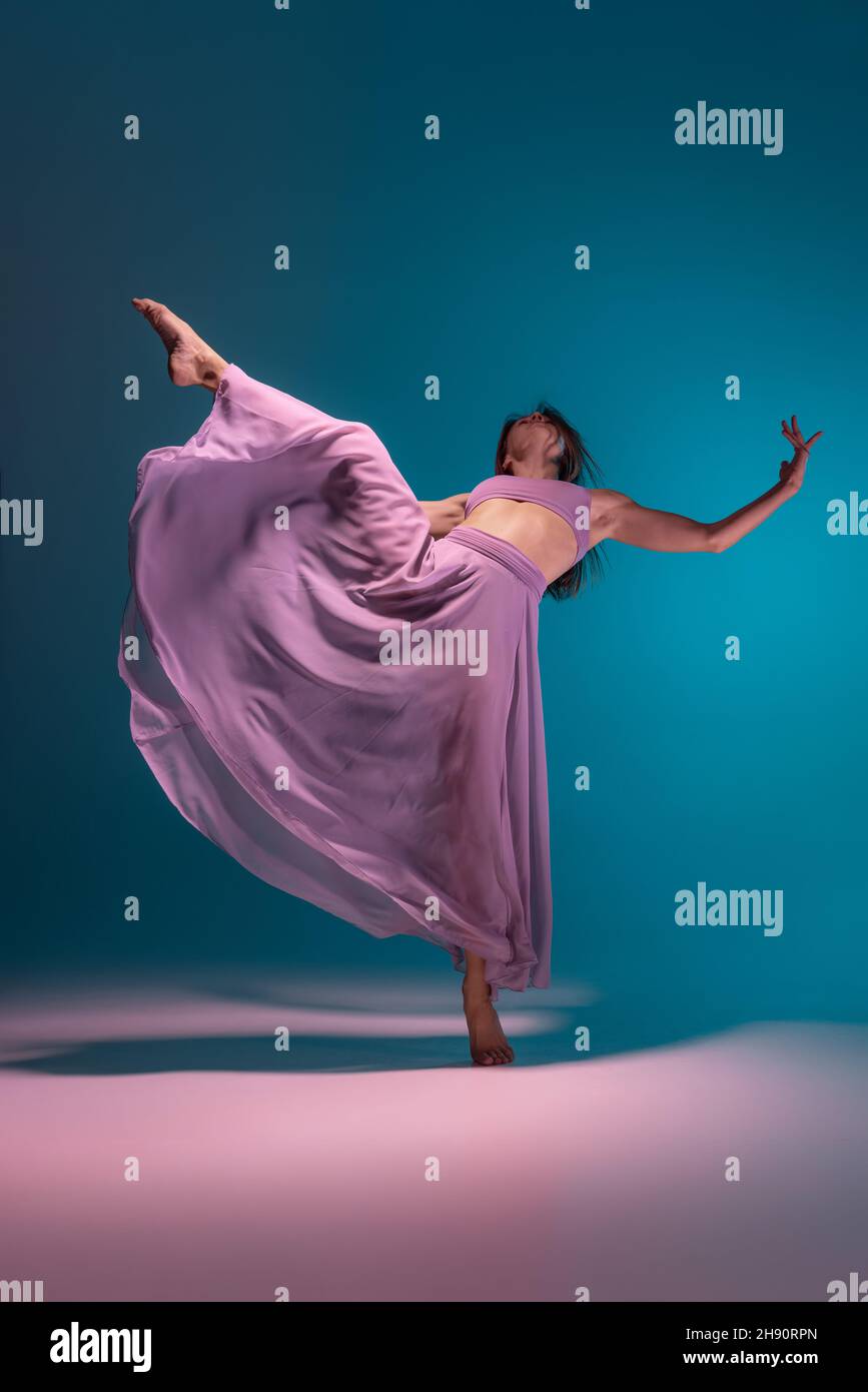 Young adorable flexible contemp dancer in lilac dress dancing isolated on gradient blue white background in neon. Stock Photo