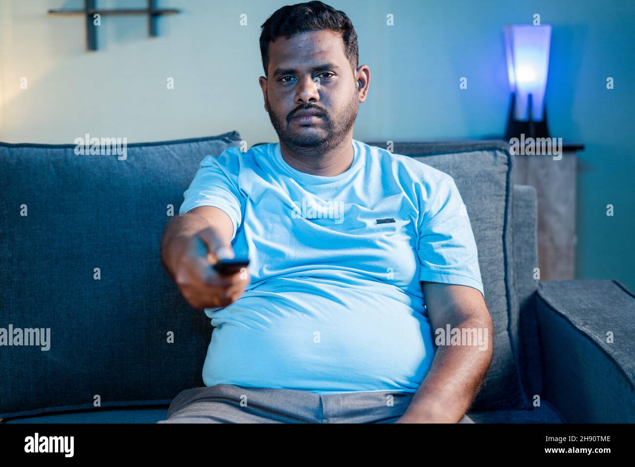 Obese Indian fat man watching tv during weekend at home - concept of boredom, laziness and relaxation or leisure activities. Stock Photo