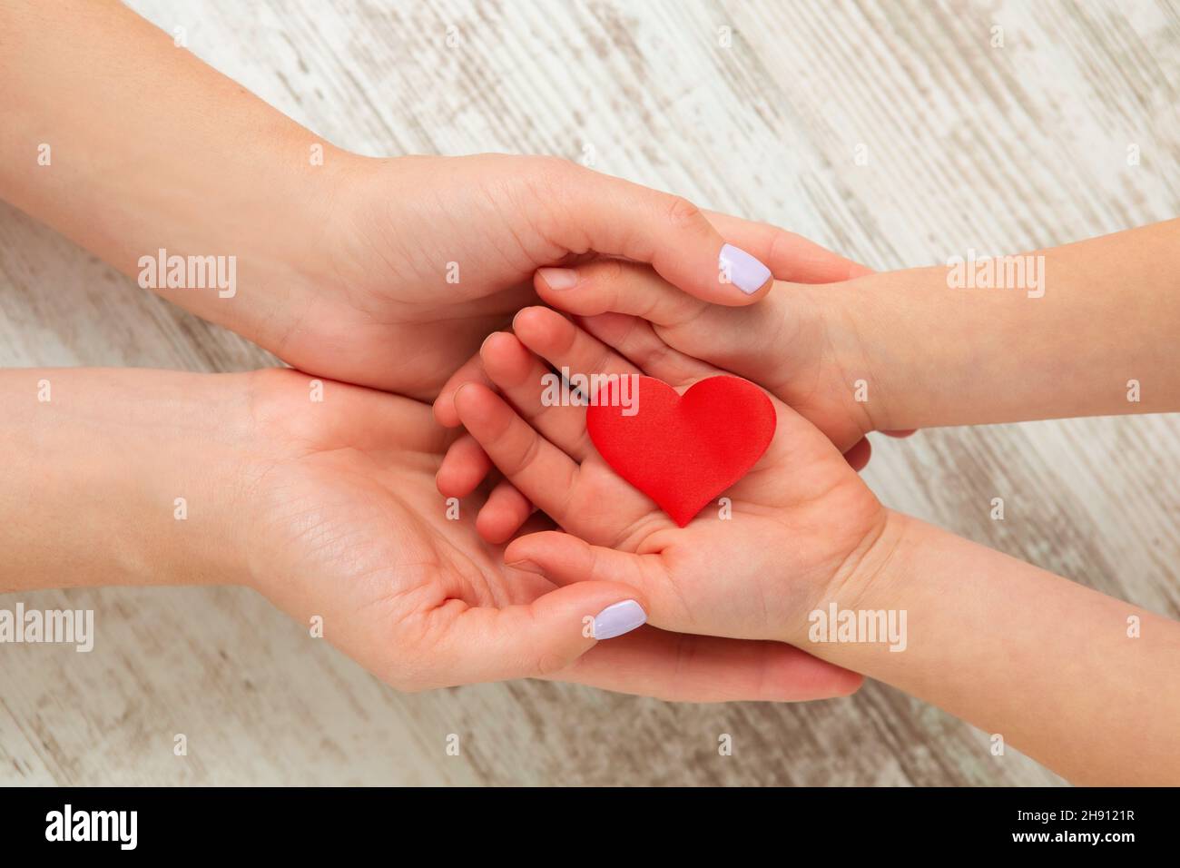 Red heart in child and mother hands on wooden background. Health care ...