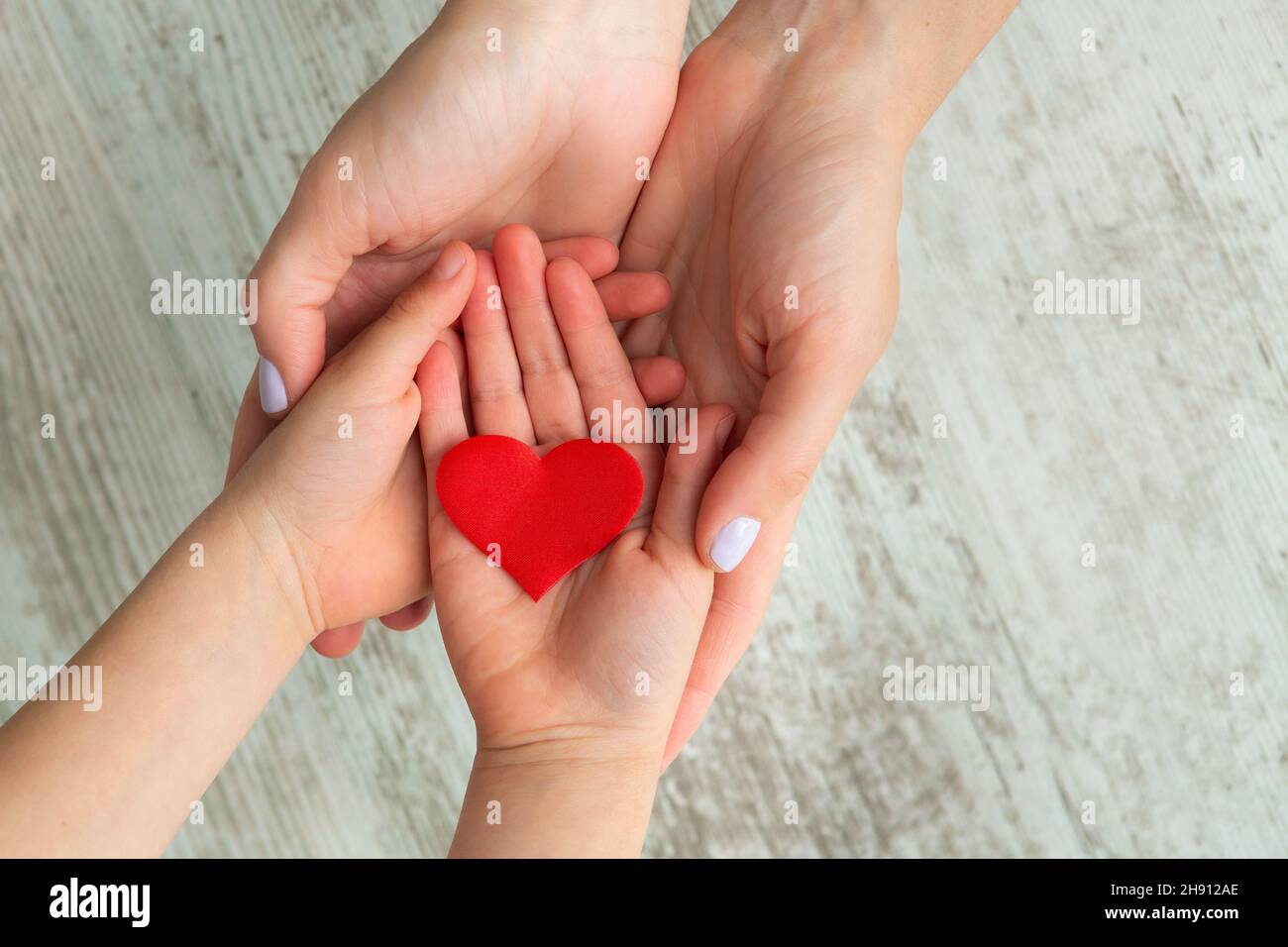 Red heart in child and mother hands on wooden background. Health care ...