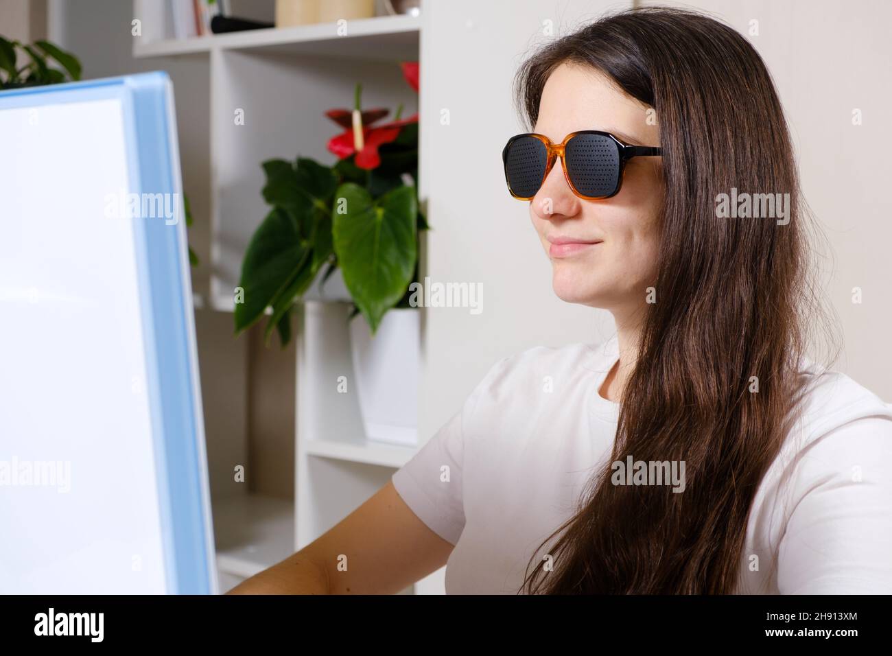 A woman looks at a computer screen through perforated glasses with
