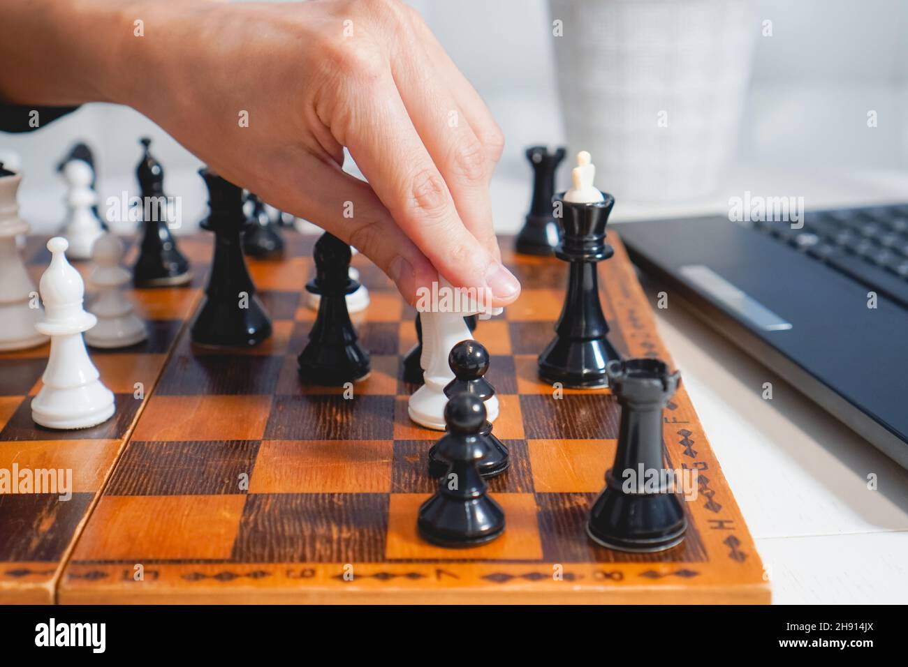 Man plays chess on wooden board near laptop. Top view. Selective focus. Strategy and competition concept Stock Photo