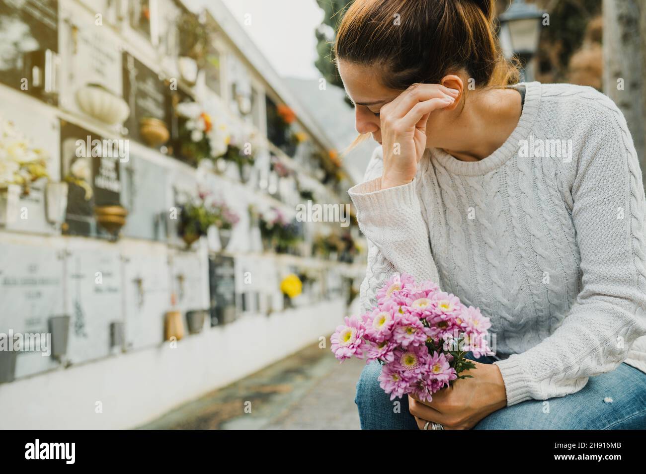 Woman with flowers crying near columbarium wall in cemetery Stock Photo